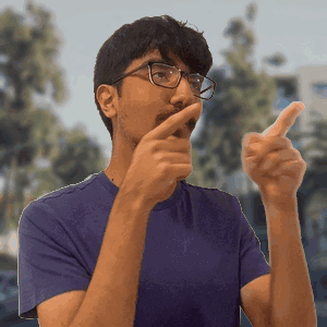 A Man Wearing Glasses And A Purple Shirt Is Pointing His Finger GIF