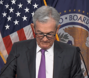 A Man Wearing Glasses And A Purple Tie Stands In Front Of A Microphone In Front Of A Flag That Says Board GIF