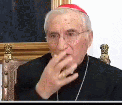 A Man Wearing Glasses And A Red Hat Is Sitting In A Chair Covering His Mouth With His Hand . GIF
