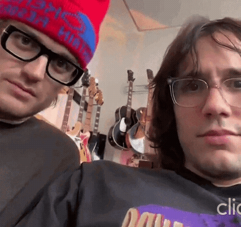 A Man Wearing Glasses And A Red Hat Is Standing Next To Another Man Wearing Glasses And A Hat . GIF
