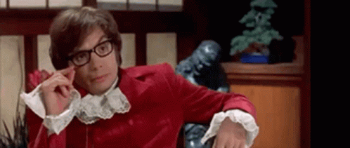 A Man Wearing Glasses And A Red Jacket Is Sitting In A Chair In A Room . GIF
