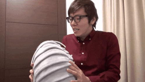 A Man Wearing Glasses And A Red Shirt Is Holding A Large Object GIF