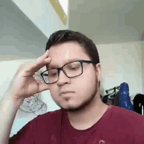 A Man Wearing Glasses And A Red Shirt Is Holding His Hand To His Head . GIF