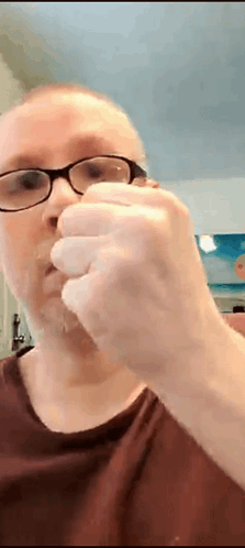 A Man Wearing Glasses And A Red Shirt Is Holding Something In His Hand GIF