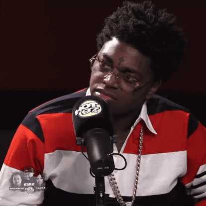 A Man Wearing Glasses And A Red White And Blue Shirt Stands In Front Of A Radio Microphone GIF