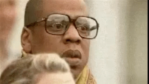 A Man Wearing Glasses And A Scarf Is Looking At A Woman . GIF