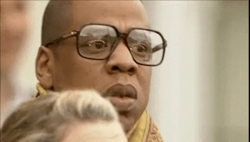 A Man Wearing Glasses And A Scarf Is Looking At Another Man . GIF
