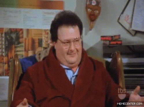 A Man Wearing Glasses And A Scarf Is Sitting In A Chair GIF