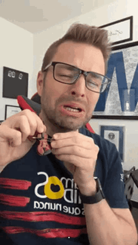 A Man Wearing Glasses And A Shirt That Says 200 On It Is Holding Something In His Hands GIF