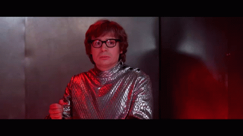 A Man Wearing Glasses And A Silver Shirt Is Pointing At The Camera GIF