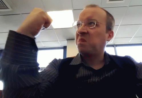 A Man Wearing Glasses And A Striped Shirt Holds His Fist Up In The Air GIF