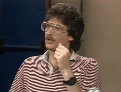 A Man Wearing Glasses And A Striped Shirt Holds His Hand To His Chin GIF