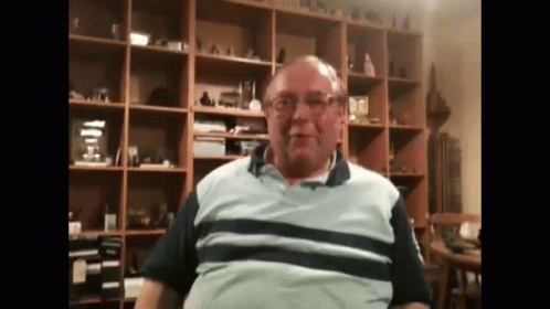 a man wearing glasses and a striped shirt is sitting in front of a bookshelf .