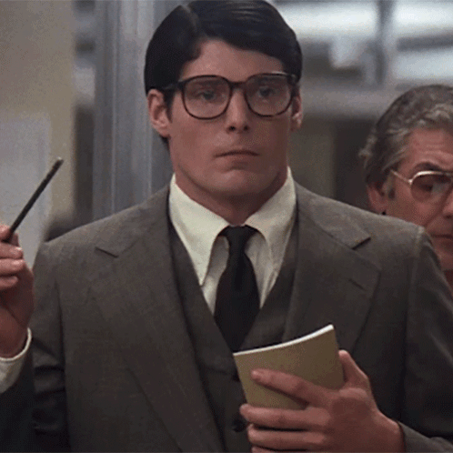 A Man Wearing Glasses And A Suit Is Holding A Notebook GIF