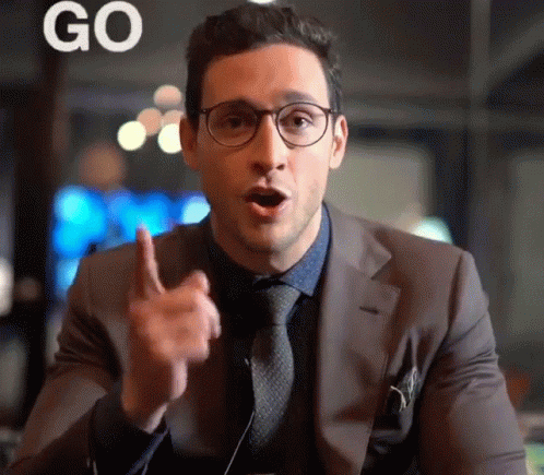 A Man Wearing Glasses And A Suit Is Pointing Up With The Word Go Behind Him GIF