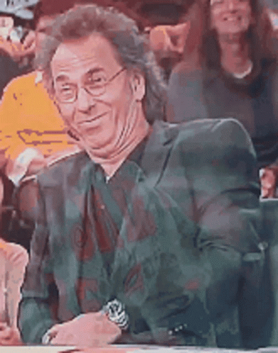 A Man Wearing Glasses And A Suit Is Sitting In A Crowd . GIF