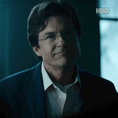 A Man Wearing Glasses And A Suit Is Smiling In Front Of A Hbo Logo GIF