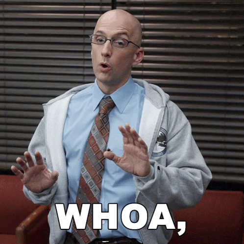 A Man Wearing Glasses And A Tie Is Sitting In A Chair And Says Whoa GIF