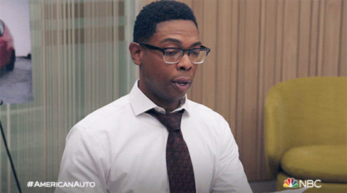 a man wearing glasses and a tie is sitting in front of a yellow chair ..