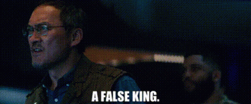 A Man Wearing Glasses And A Vest Is Standing In A Dark Room . GIF