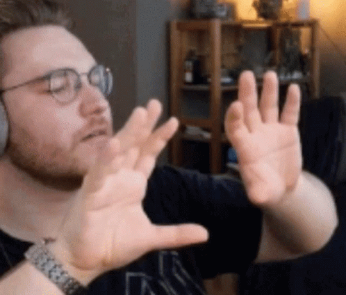 A Man Wearing Glasses And A Watch Is Making A Funny Face With His Hands GIF