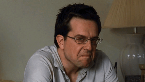A Man Wearing Glasses And A White Shirt Is Making A Face GIF