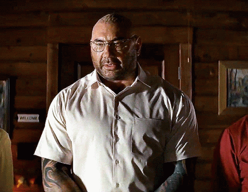 A Man Wearing Glasses And A White Shirt Stands In Front Of A Sign That Says Welcome GIF