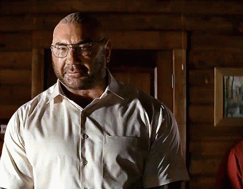 A Man Wearing Glasses And A White Shirt Stands In Front Of A Wooden Door GIF