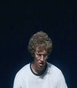 A Man Wearing Glasses And A White Shirt That Says Vote For Is Making A Funny Face . GIF