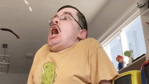 A Man Wearing Glasses And A Yellow T-Shirt With A Dinosaur On It GIF