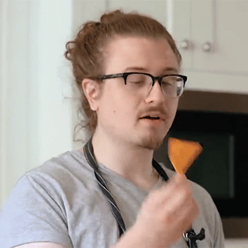 A Man Wearing Glasses And An Apron Is Eating A Chip GIF
