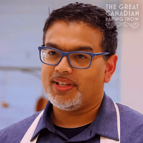 a man wearing glasses and an apron is featured in the great canadian baking show