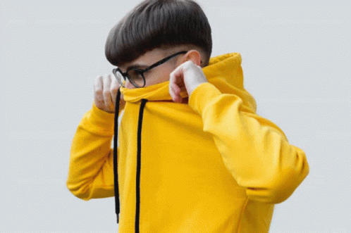 A Man Wearing Glasses And An Orange Hoodie Adjusts His Hood GIF