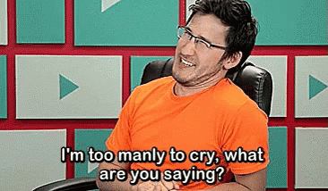 A Man Wearing Glasses And An Orange Shirt Is Sitting In A Chair And Laughing . GIF