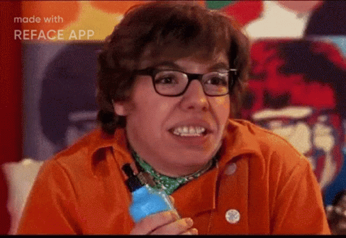 A Man Wearing Glasses And An Orange Shirt Is Smiling And Holding A Blue Bottle . GIF