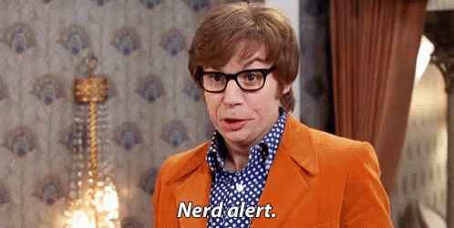 A Man Wearing Glasses And An Orange Suit Is Standing In A Room And Says Nerd Alert . GIF