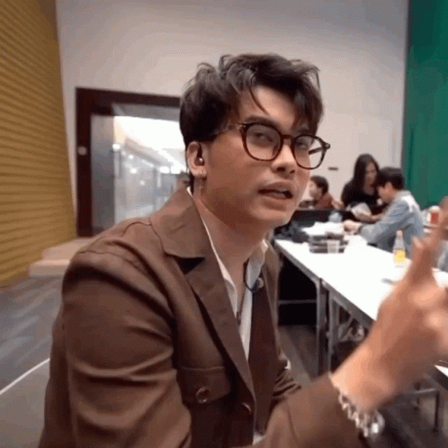 A Man Wearing Glasses And Ear Buds Is Sitting In Front Of A Table GIF