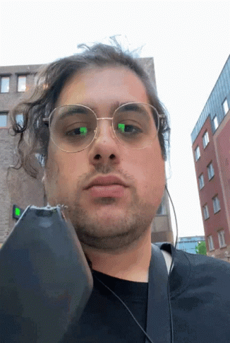 A Man Wearing Glasses And Headphones Holds A Cell Phone In Front Of His Face GIF