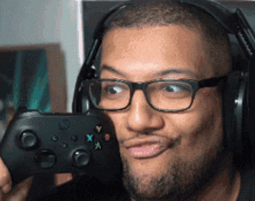 A Man Wearing Glasses And Headphones Is Holding A Video Game Controller And Making A Funny Face GIF