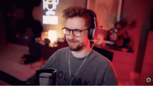 A Man Wearing Glasses And Headphones Is Standing In Front Of A Microphone . GIF