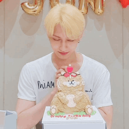 A Man Wearing Glasses Blows Out A Pink Candle On Top Of A Cat Cake GIF