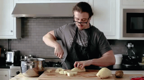 A Man Wearing Glasses Is Cutting Potatoes On A Wooden Cutting Board GIF