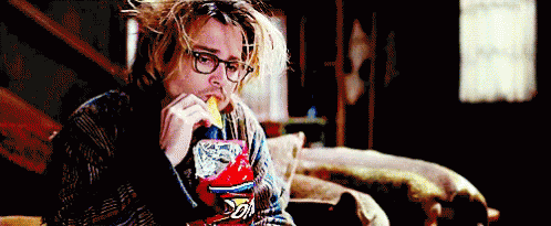 A Man Wearing Glasses Is Eating A Bag Of Doritos Chips While Sitting On A Couch . GIF