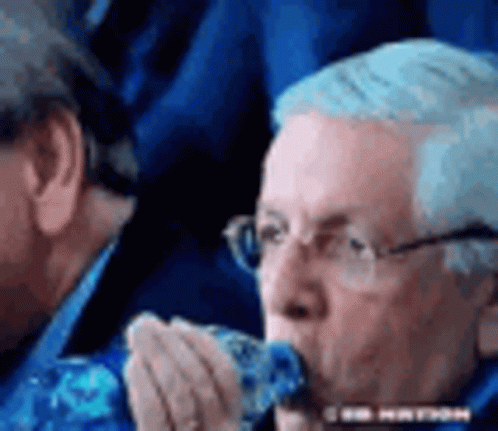 A Man Wearing Glasses Is Eating A Piece Of Food While Sitting In A Stadium . GIF