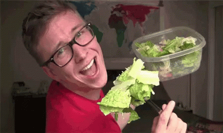 A Man Wearing Glasses Is Eating Lettuce From A Plastic Container With Chopsticks . GIF
