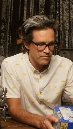 A Man Wearing Glasses Is Holding A Box Of 16 Value Pack GIF