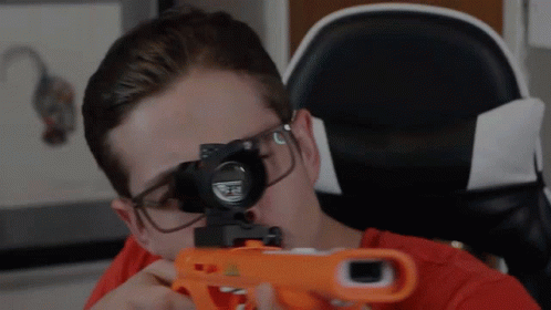A Man Wearing Glasses Is Holding A Nerf Gun In Front Of His Face GIF