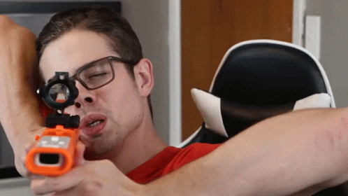 A Man Wearing Glasses Is Holding A Toy Gun In His Hand GIF