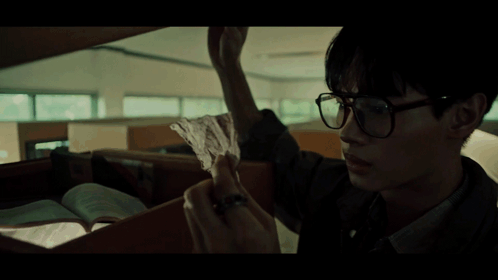 A Man Wearing Glasses Is Holding Another Man 'S Hand In A Dark Room GIF