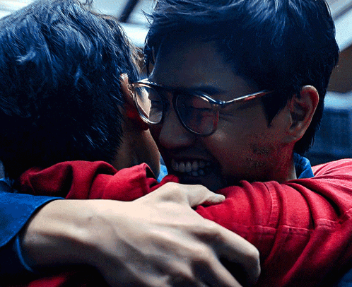 A Man Wearing Glasses Is Hugging Another Man Wearing A Red Shirt GIF